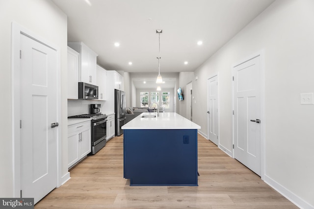 kitchen featuring appliances with stainless steel finishes, decorative light fixtures, a kitchen island with sink, and white cabinetry