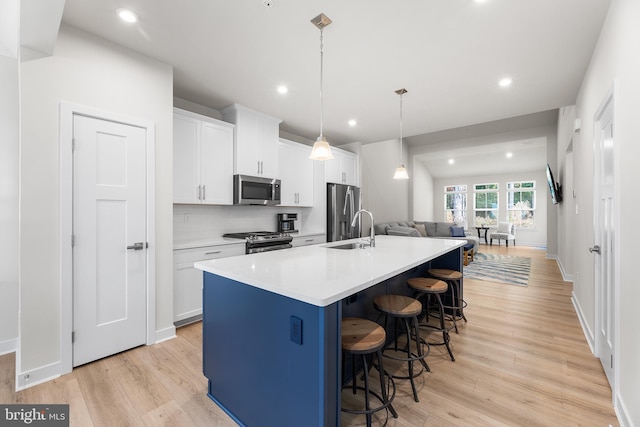 kitchen with an island with sink, white cabinets, decorative light fixtures, light wood-type flooring, and appliances with stainless steel finishes