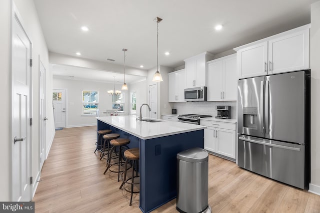 kitchen featuring appliances with stainless steel finishes, white cabinetry, decorative light fixtures, light hardwood / wood-style flooring, and a center island with sink