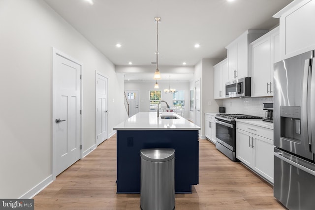 kitchen featuring white cabinets, appliances with stainless steel finishes, decorative light fixtures, and a kitchen island with sink