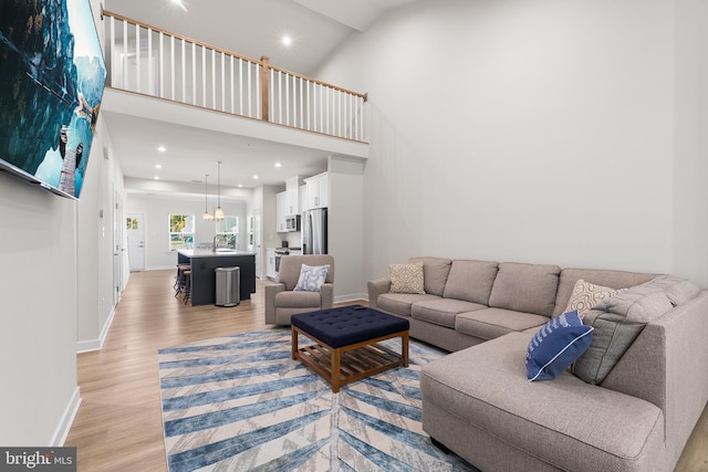 living room featuring light hardwood / wood-style floors, a notable chandelier, a towering ceiling, and sink