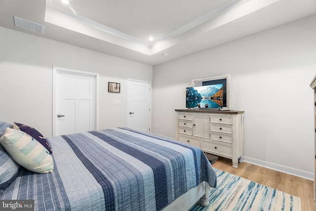 bedroom with light hardwood / wood-style floors and a raised ceiling