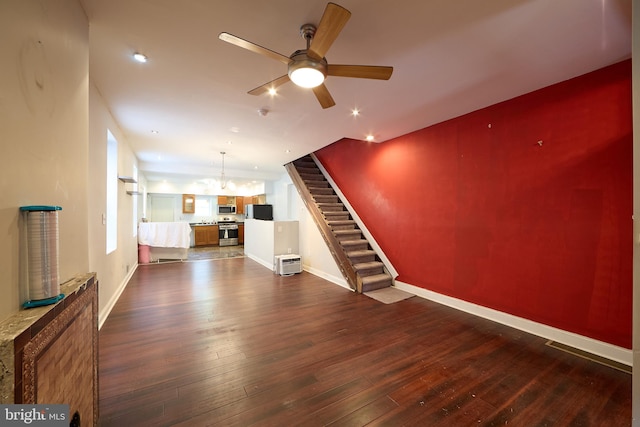 unfurnished living room featuring ceiling fan with notable chandelier and dark hardwood / wood-style floors