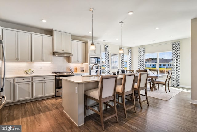 kitchen with dark hardwood / wood-style flooring, stainless steel appliances, pendant lighting, a breakfast bar, and a kitchen island with sink