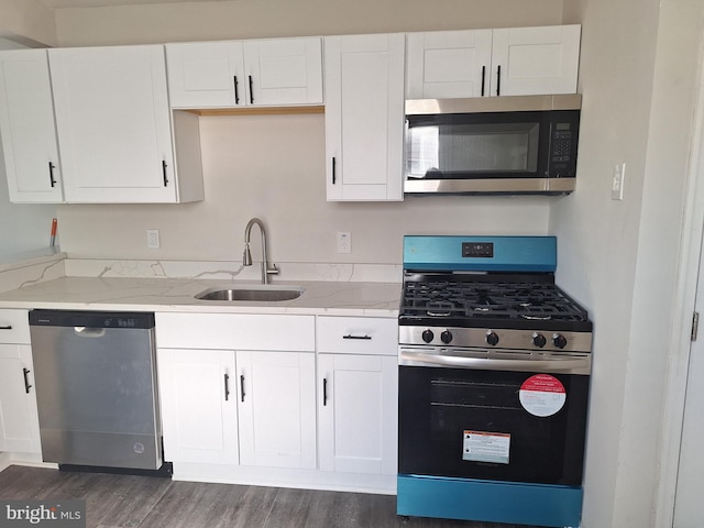 kitchen featuring white cabinets, light stone counters, appliances with stainless steel finishes, dark wood-type flooring, and sink