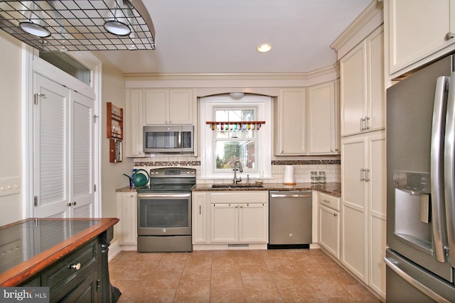 kitchen with backsplash, sink, hanging light fixtures, cream cabinetry, and stainless steel appliances