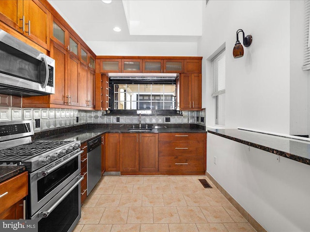 kitchen featuring dark stone counters, decorative backsplash, light tile patterned flooring, and stainless steel appliances