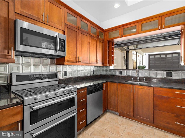 kitchen featuring decorative backsplash, stainless steel appliances, sink, light tile patterned floors, and dark stone countertops