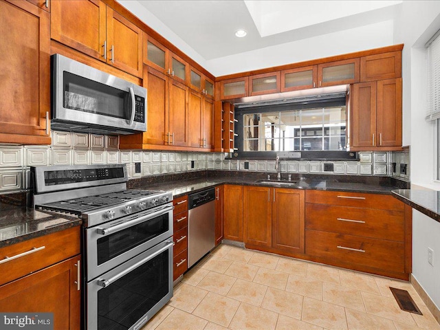 kitchen with decorative backsplash, sink, stainless steel appliances, and dark stone countertops