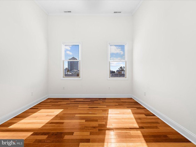 empty room with visible vents, wood finished floors, baseboards, and ornamental molding
