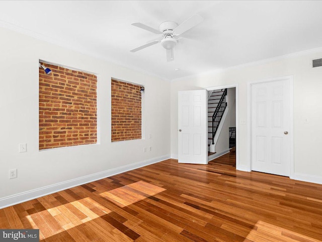 spare room featuring baseboards, ornamental molding, ceiling fan, visible vents, and wood finished floors