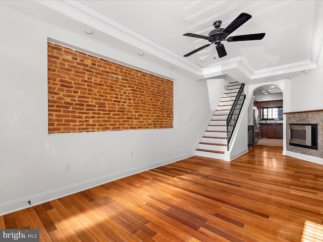 unfurnished living room with ceiling fan, brick wall, crown molding, hardwood / wood-style floors, and a tray ceiling