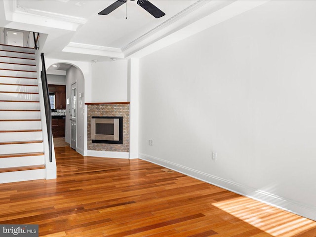 unfurnished living room with ceiling fan, a raised ceiling, wood-type flooring, and a fireplace