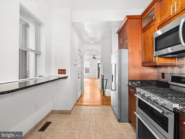 kitchen with dark stone countertops, ceiling fan, light hardwood / wood-style flooring, and appliances with stainless steel finishes