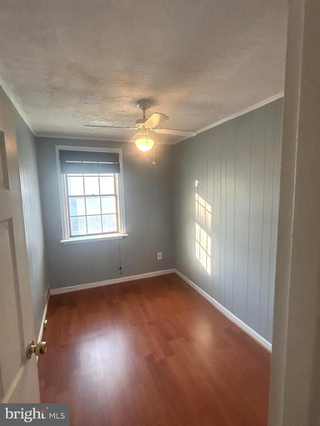 empty room featuring a textured ceiling, ceiling fan, wood walls, and hardwood / wood-style flooring