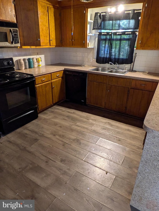 kitchen with black appliances, backsplash, sink, and hardwood / wood-style flooring