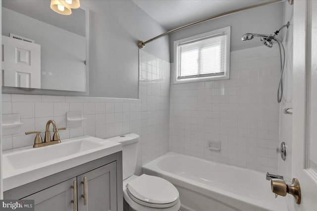 full bathroom with toilet, tiled shower / bath combo, vanity, and tile walls