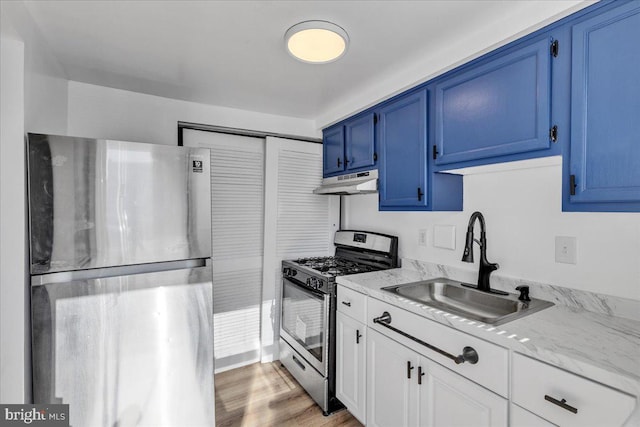 kitchen with appliances with stainless steel finishes, white cabinetry, blue cabinetry, light hardwood / wood-style flooring, and sink