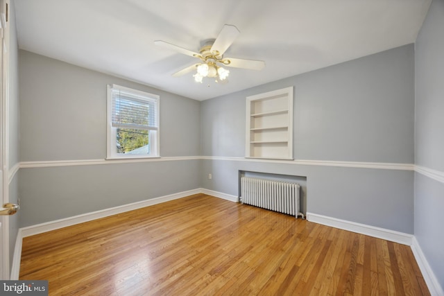 spare room featuring radiator heating unit, ceiling fan, built in features, and light wood-type flooring