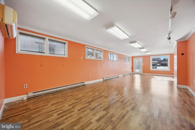 spare room featuring a wall mounted air conditioner, crown molding, baseboard heating, and wood-type flooring