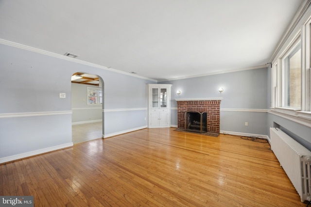 unfurnished living room with a wealth of natural light, crown molding, light wood-type flooring, and radiator