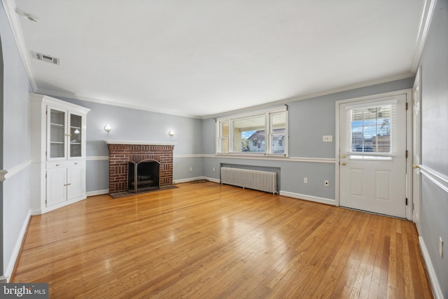 unfurnished living room with crown molding, a brick fireplace, radiator heating unit, and light wood-type flooring