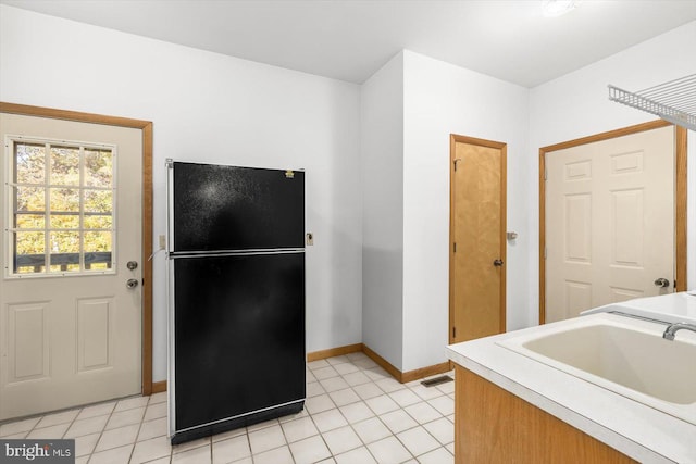 kitchen with sink, light tile patterned floors, and black fridge