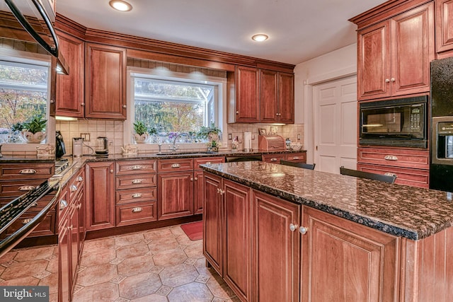 kitchen featuring sink, a kitchen island, backsplash, dark stone countertops, and black microwave