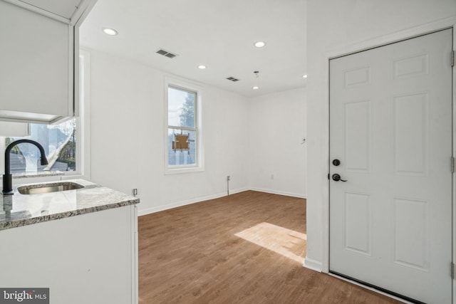 interior space featuring white cabinetry, sink, light stone counters, and light hardwood / wood-style flooring