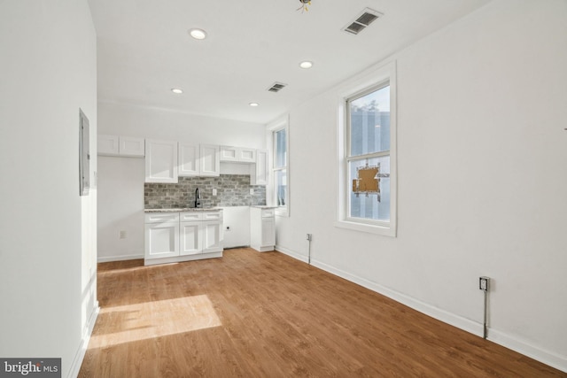 kitchen with tasteful backsplash, electric panel, light wood-type flooring, sink, and white cabinets