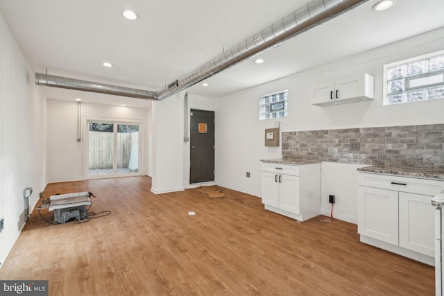 kitchen with white cabinets, light stone countertops, light hardwood / wood-style flooring, and backsplash