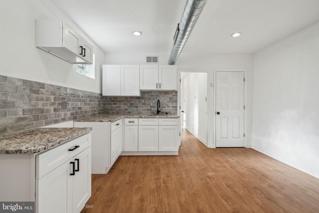 kitchen with light hardwood / wood-style floors, white cabinets, sink, backsplash, and light stone countertops