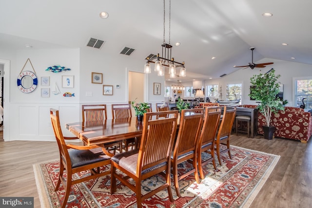 dining space with vaulted ceiling, ceiling fan with notable chandelier, and light hardwood / wood-style floors