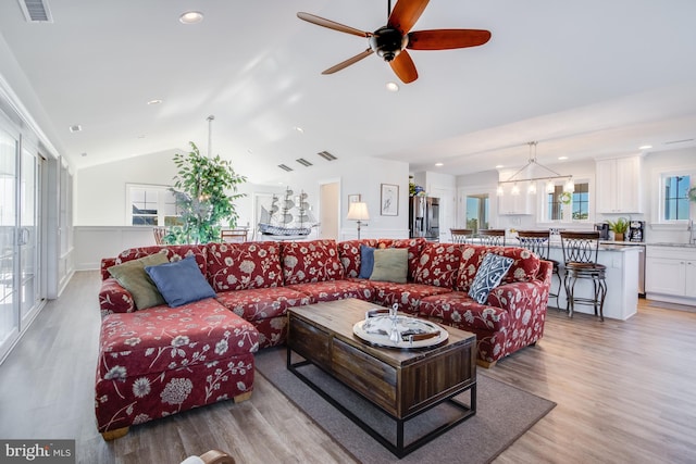 living room featuring lofted ceiling, ceiling fan with notable chandelier, and light wood-type flooring