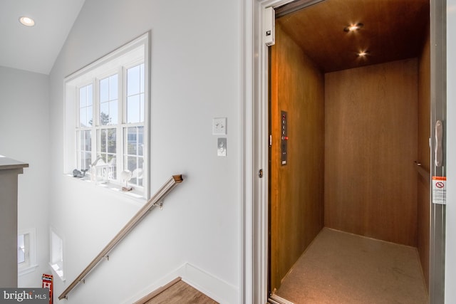 staircase with lofted ceiling, hardwood / wood-style floors, and elevator