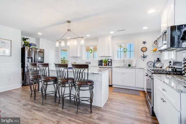 kitchen featuring a center island, stainless steel appliances, pendant lighting, white cabinets, and light hardwood / wood-style flooring