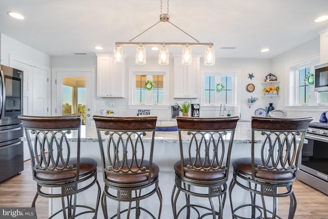 kitchen with plenty of natural light, appliances with stainless steel finishes, pendant lighting, and white cabinets