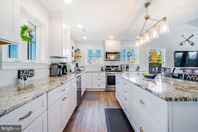 kitchen with wood-type flooring, sink, hanging light fixtures, white cabinetry, and stainless steel appliances