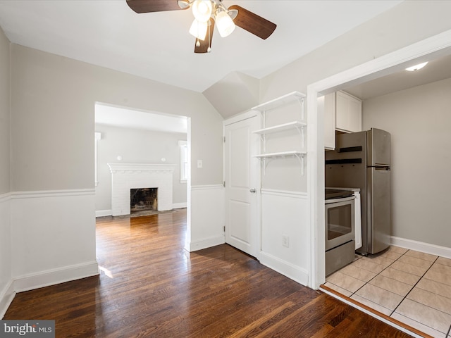 kitchen with a fireplace, white cabinetry, ceiling fan, stainless steel appliances, and light hardwood / wood-style flooring