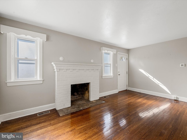 unfurnished living room with a fireplace, a healthy amount of sunlight, and dark hardwood / wood-style flooring