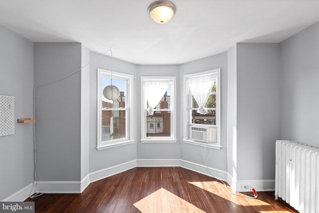 unfurnished room with cooling unit, radiator heating unit, a healthy amount of sunlight, and dark wood-type flooring