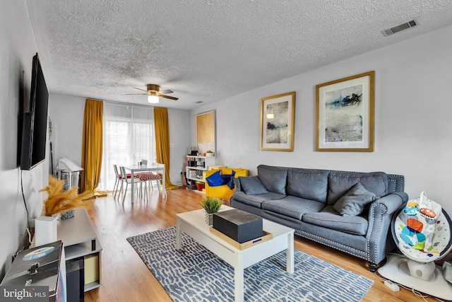 living room featuring ceiling fan, light hardwood / wood-style flooring, and a textured ceiling