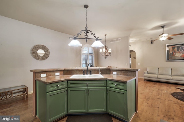 kitchen with green cabinets, a kitchen island with sink, decorative light fixtures, and wood-type flooring