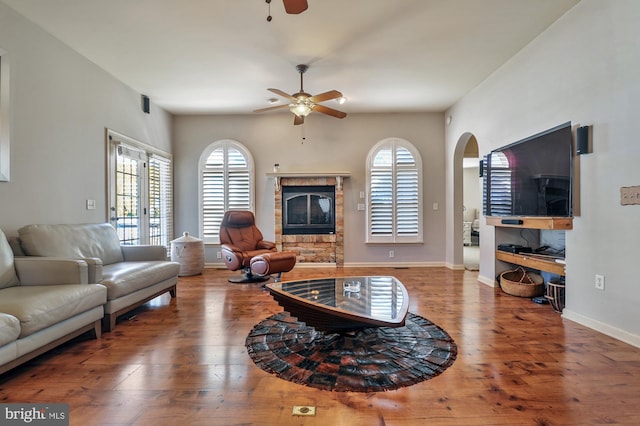 living room with a stone fireplace, hardwood / wood-style flooring, and ceiling fan