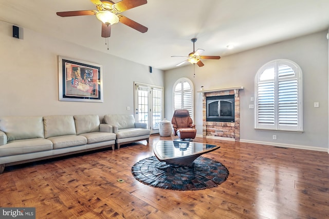 living room with ceiling fan, a stone fireplace, and hardwood / wood-style floors