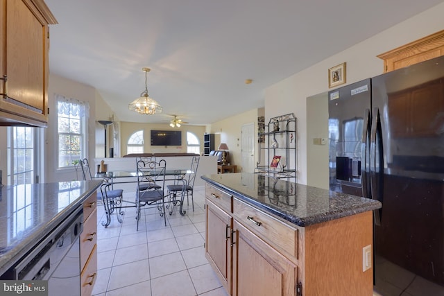 kitchen featuring a kitchen island, dark stone countertops, pendant lighting, black fridge with ice dispenser, and ceiling fan with notable chandelier