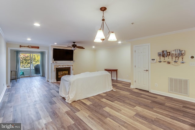 living room with crown molding, light wood-type flooring, and ceiling fan with notable chandelier