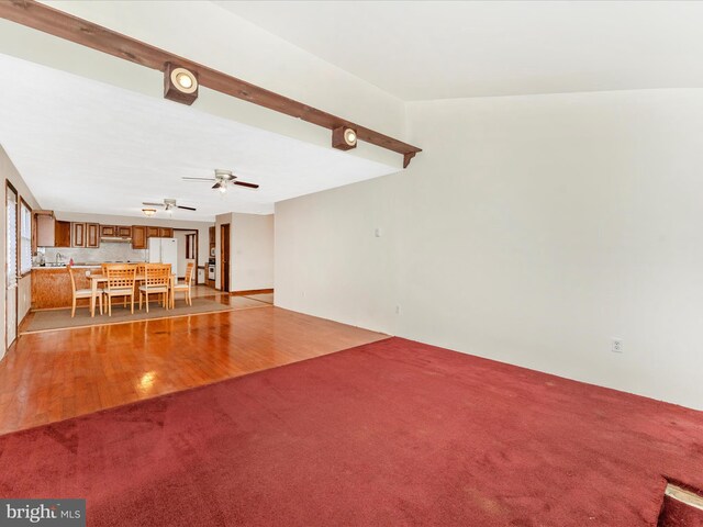 unfurnished living room featuring light hardwood / wood-style floors, beamed ceiling, and ceiling fan