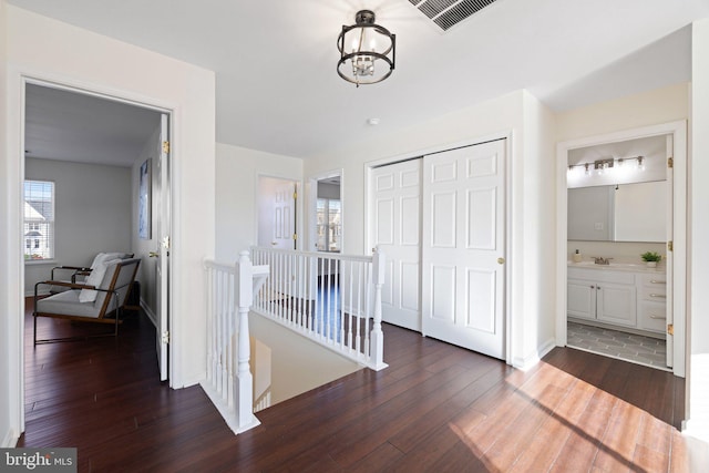 corridor featuring dark wood-type flooring, sink, and an inviting chandelier