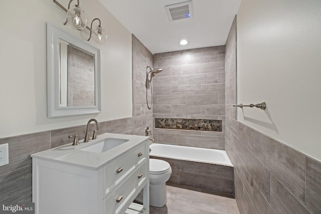 full bathroom with toilet, vanity, tiled shower / bath combo, and tile walls